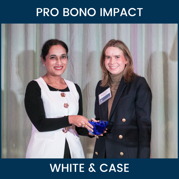 Two women hold a blue glass award bowl onstage at Ayuda’s Standing with Immigrants event. Text reads “Pro Bono Impact” and “White & Case.”