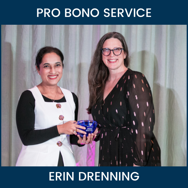 Two women hold a blue glass award bowl onstage at Ayuda’s Standing with Immigrants event. Text reads “Pro Bono Service” and “Erin Drenning.”